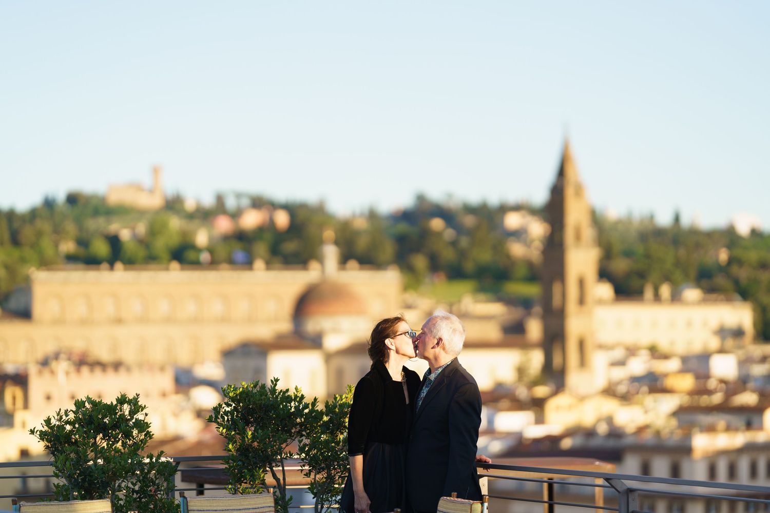 A couple enjoying a romantic moment on a rooftop terrace overlooking Florence's historic skyline at sunset.