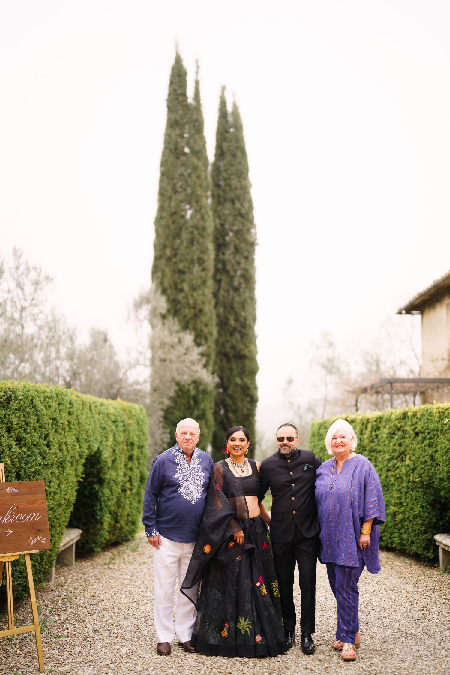 Family gathering on a gravel path lined with tall cypress trees and manicured hedges.