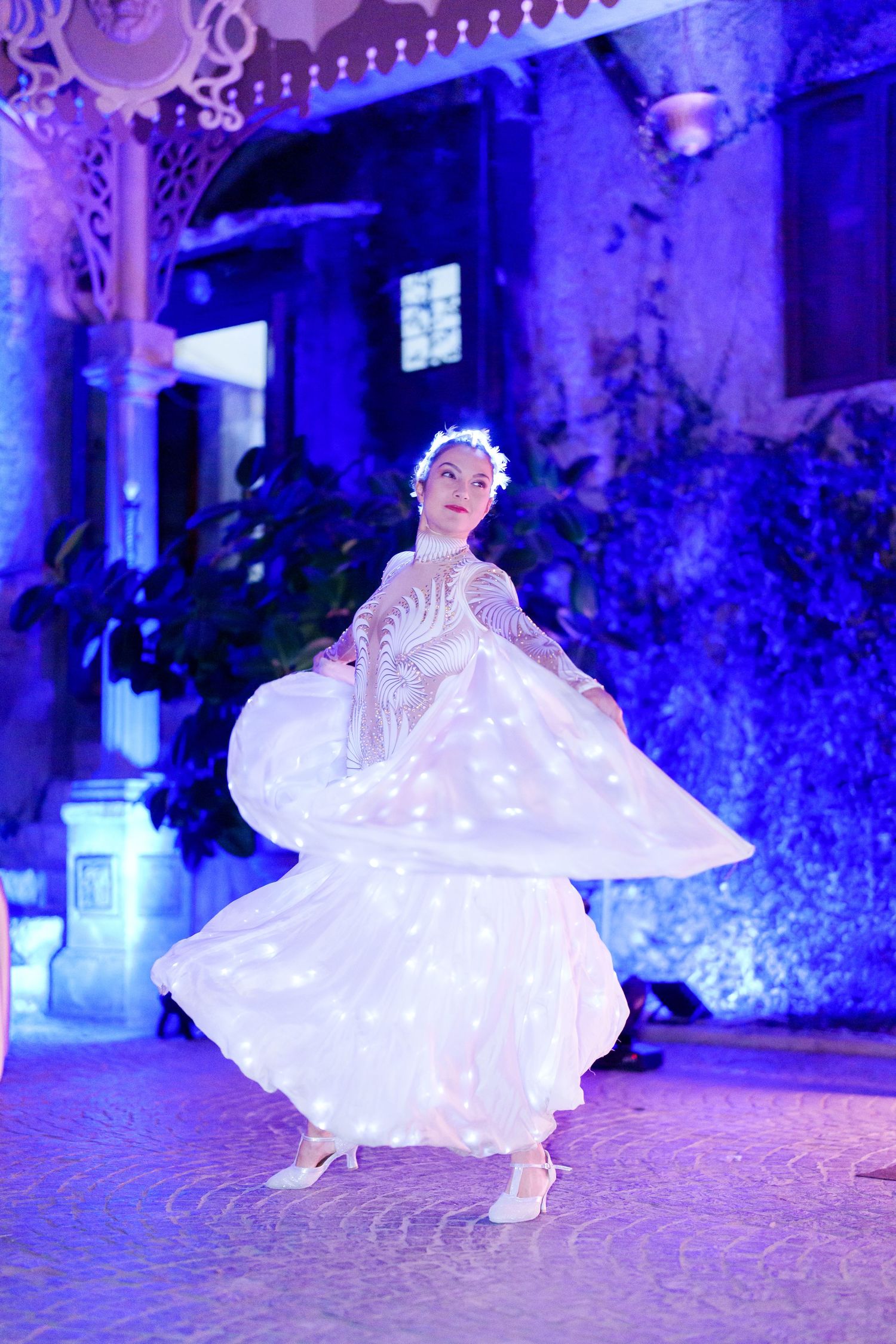 A dancer in a glowing white dress twirls gracefully under dramatic blue lighting.