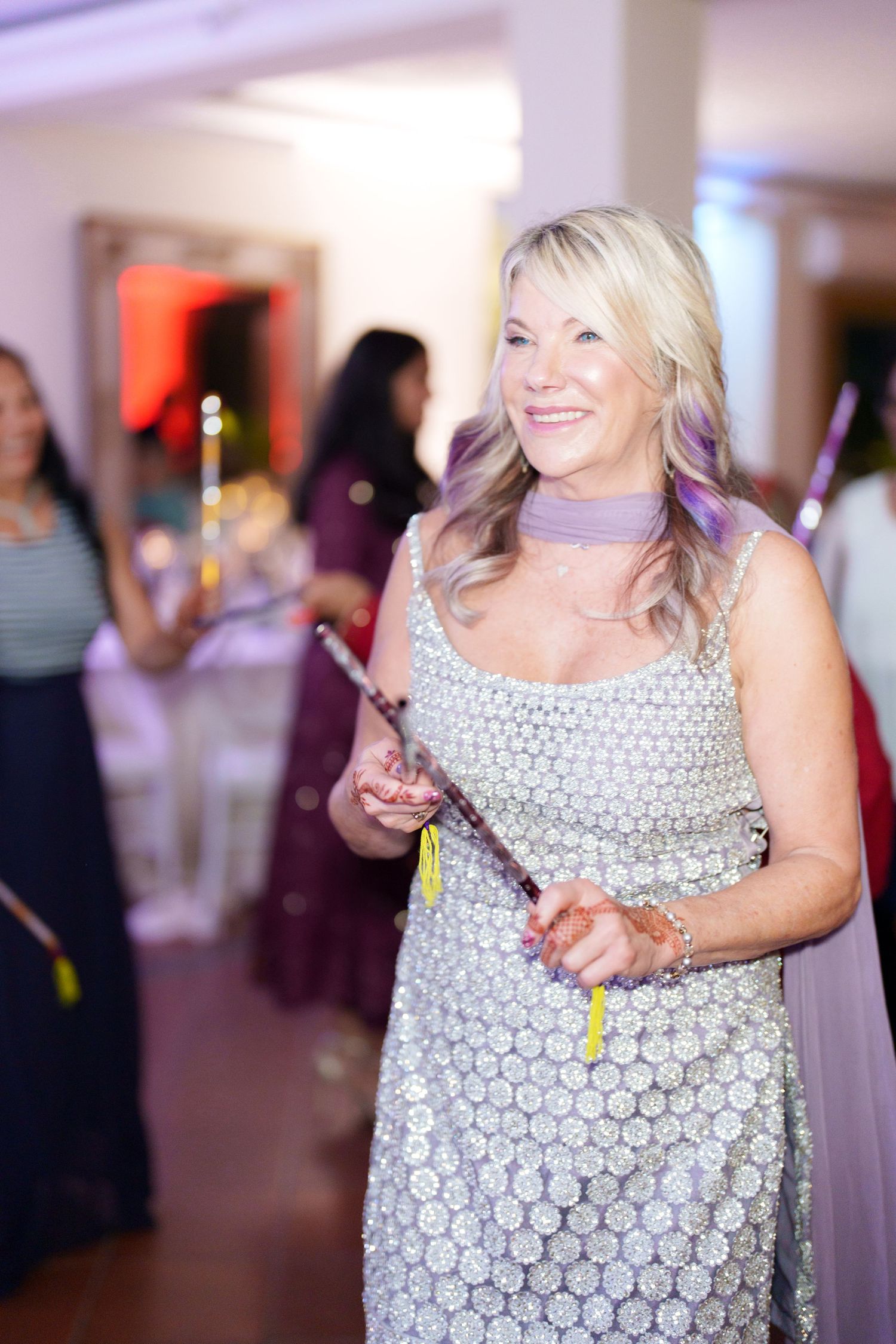 Guest in a silver sequined dress smiling while holding sparklers at an indoor party.