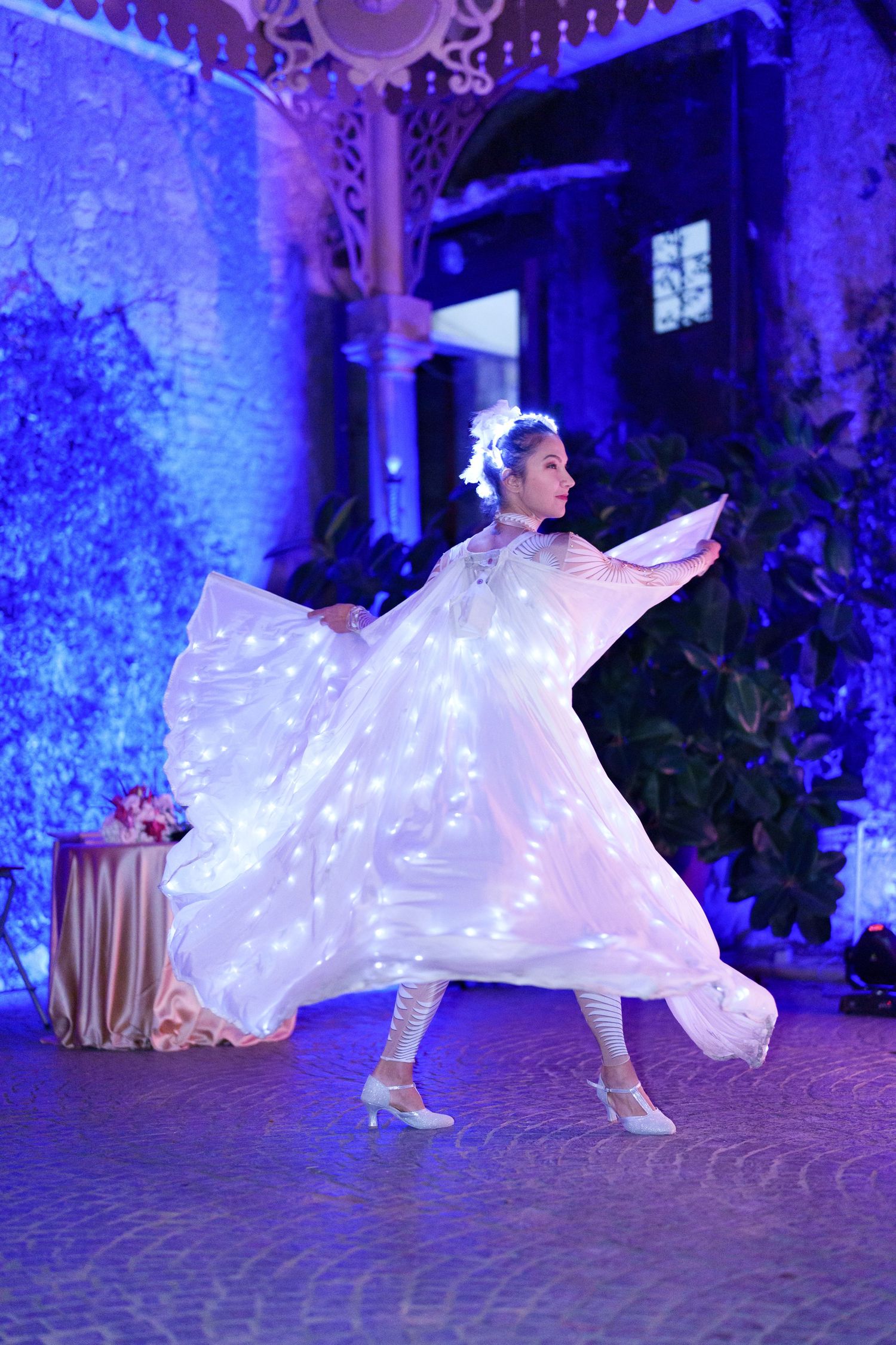A performer in an illuminated white costume spins dramatically on a cobblestone floor.