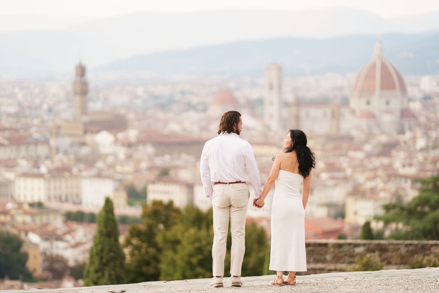 A couple enjoys a panoramic view of Florence, Italy with the iconic Duomo cathedral visible in the cityscape below.