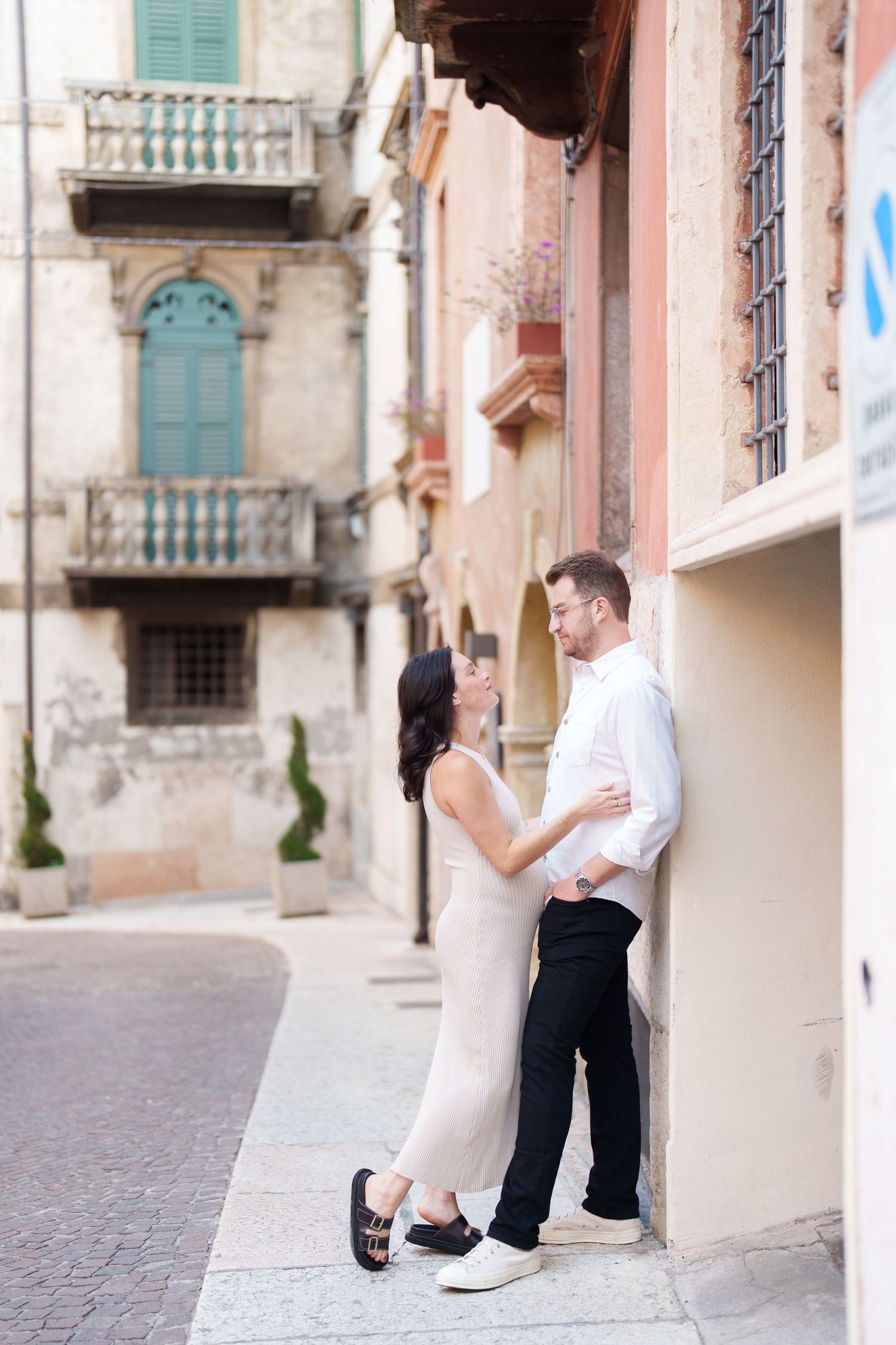 Couple shares intimate moment against pastel walls on quaint European street with vintage balconies and shutters.