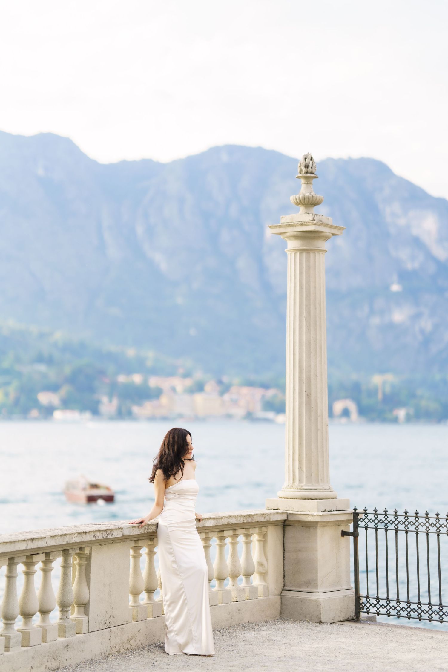 A scenic lakeside terrace with white stone columns and balustrades overlooking mountains and water in Lake Como, Italy.