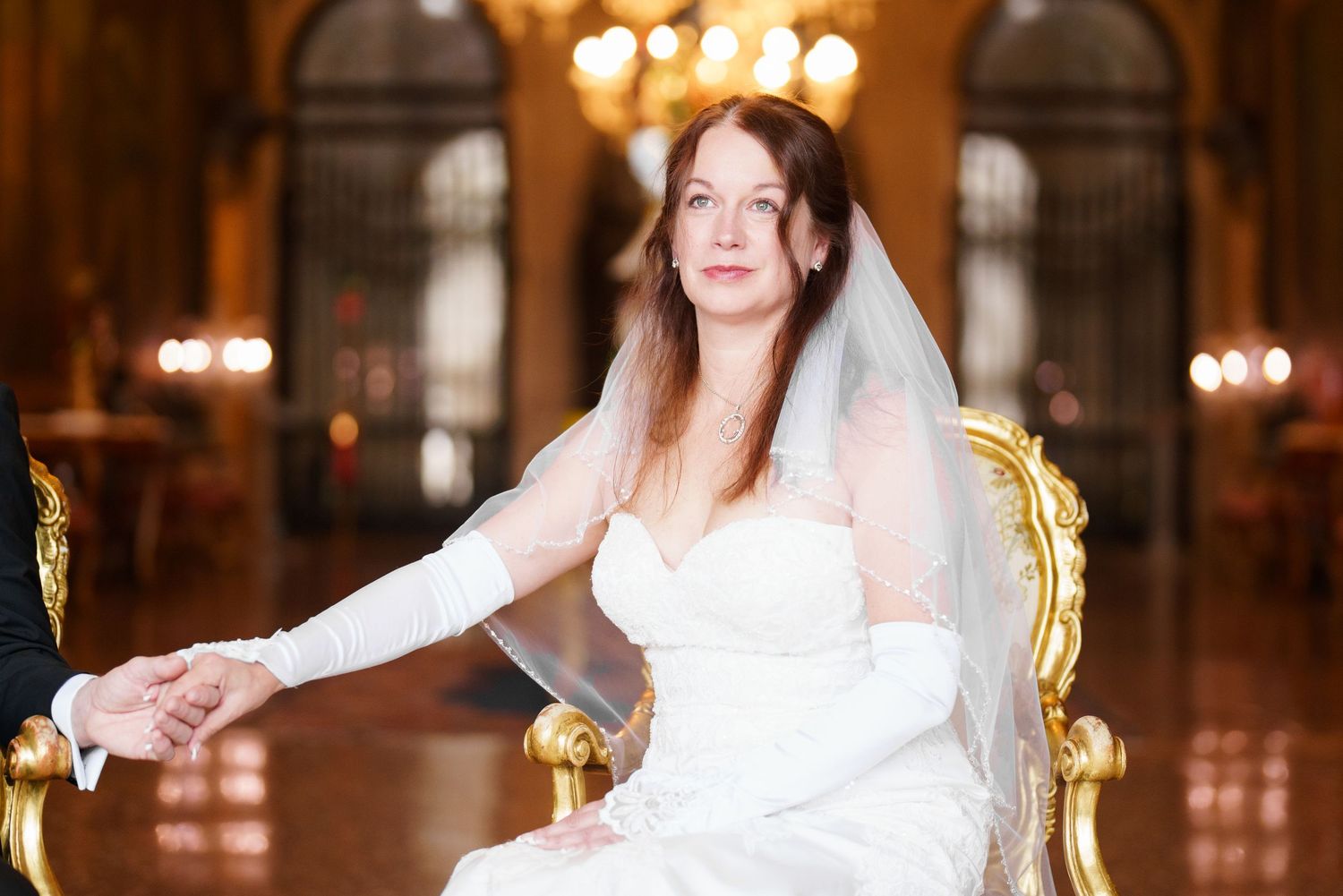 Bride and groom celebrate during their wedding reception in an elegant ballroom with warm lighting and chandeliers.
