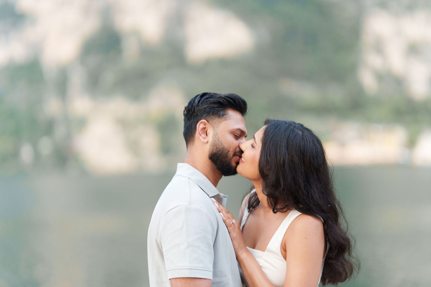 A couple shares a romantic moment during their engagement photo session near a waterfront setting.