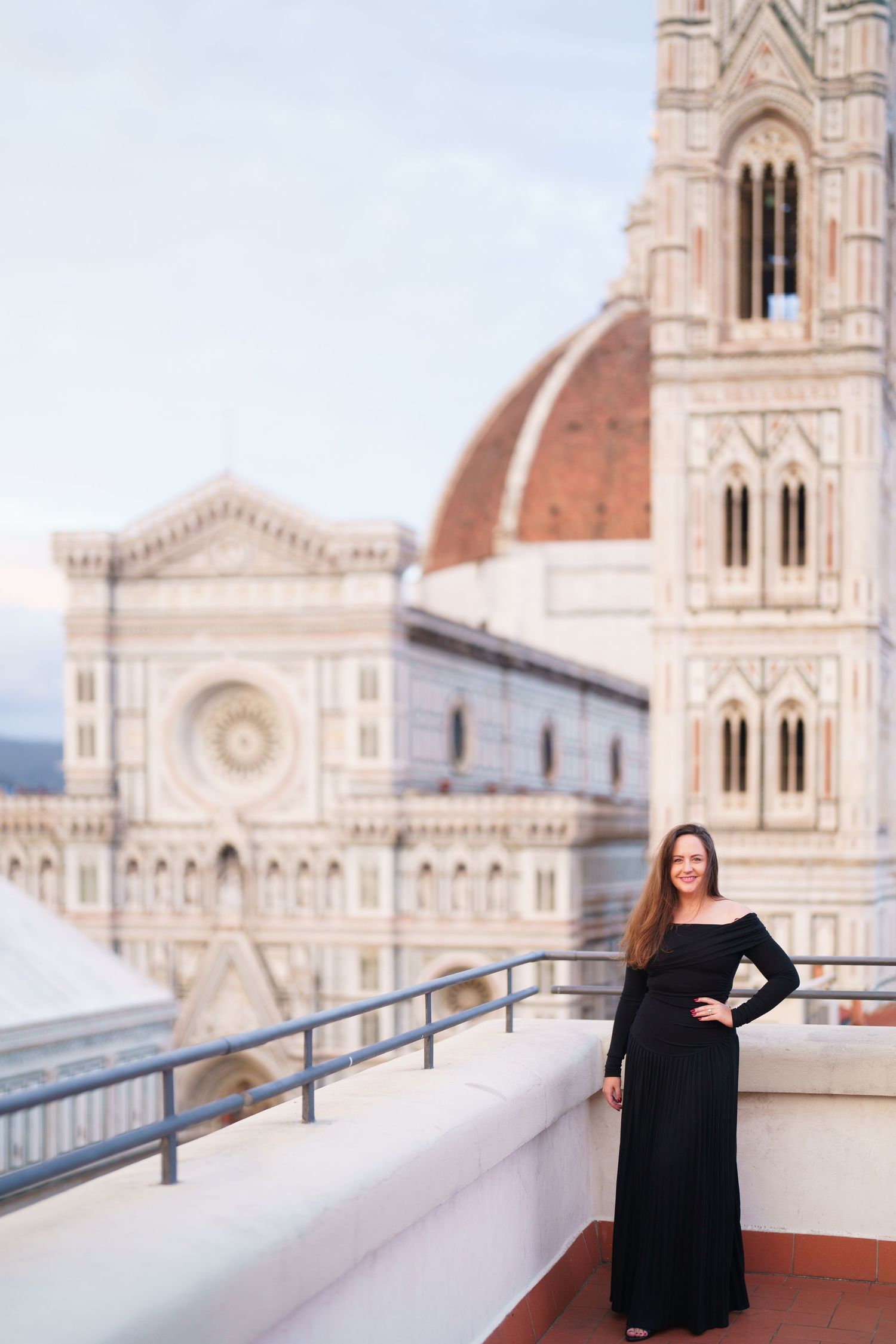 Woman in black dress poses on terrace overlooking Florence Cathedral and Brunelleschi's Dome in Italy.