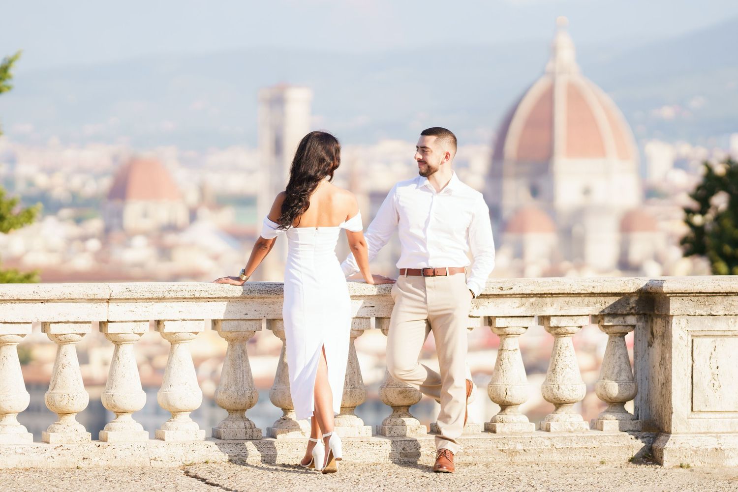 A couple in white outfits stands on a terrace overlooking Florence's iconic Duomo cathedral in Italy.