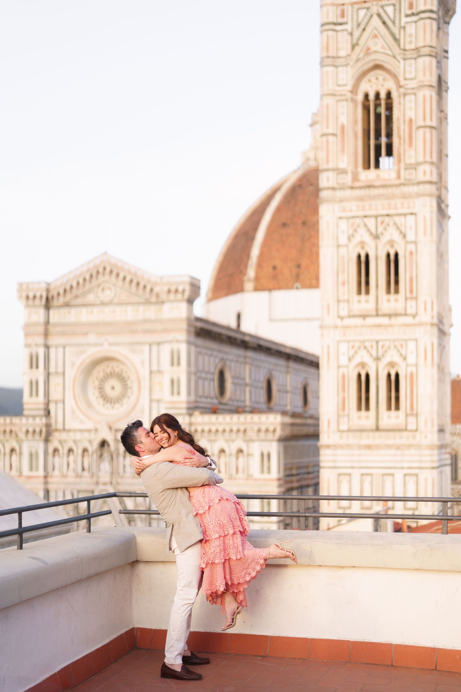 A couple shares a romantic kiss on a rooftop terrace overlooking the historic Florence Cathedral in Italy.