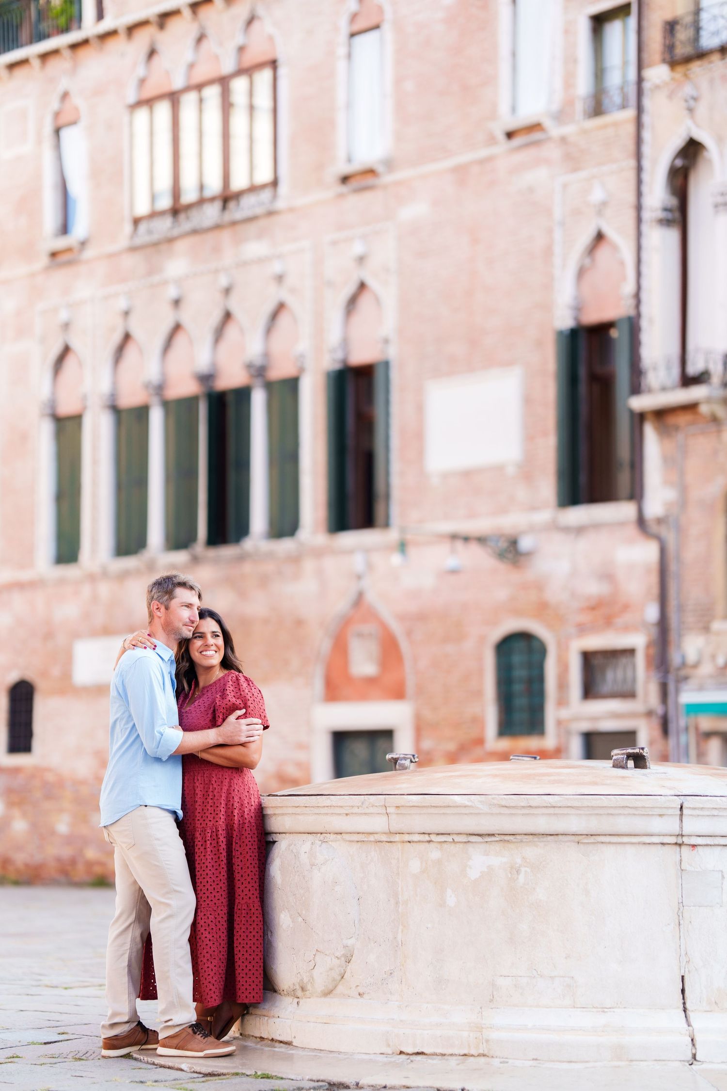 Romantic couple embracing by a stone well in Venice, Italy, with historic Gothic architecture in the background.