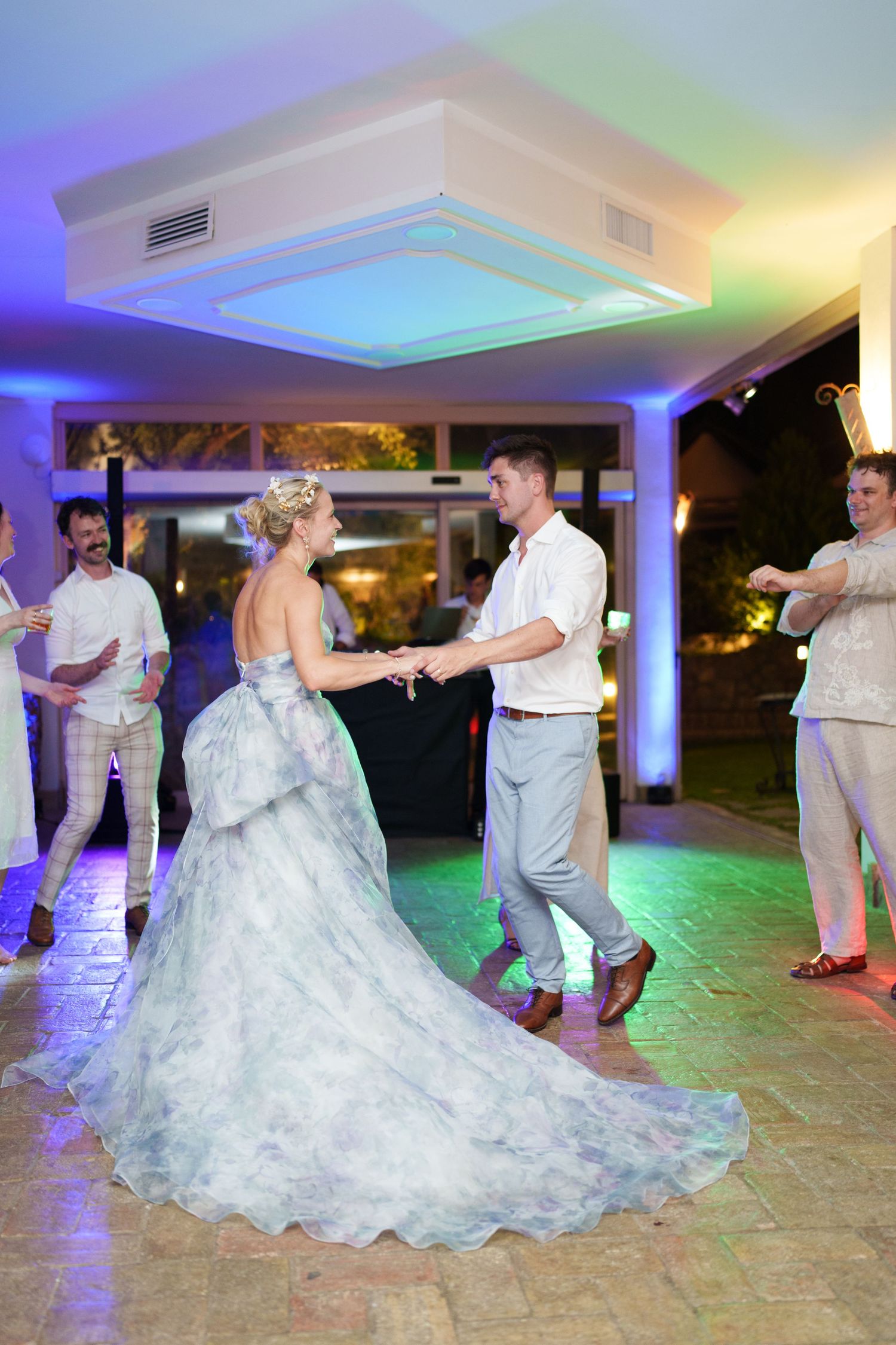 Bride and groom share first dance at wedding reception with colorful lighting and guests watching.