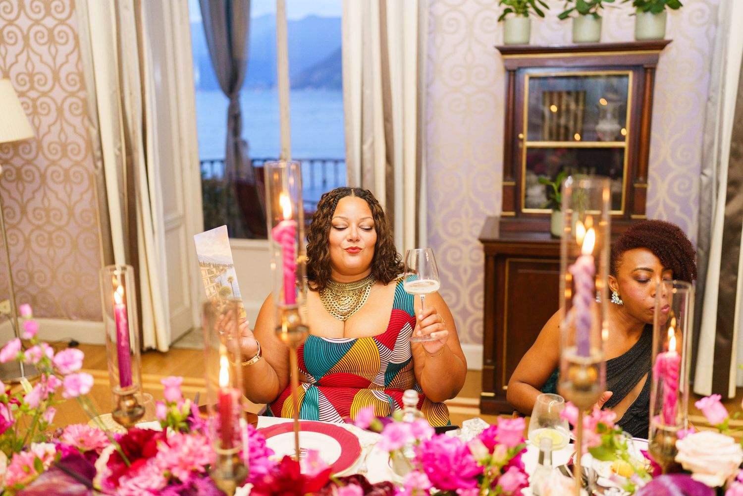 Two women sit at a elegantly decorated wedding reception table with colorful candles and floral arrangements.