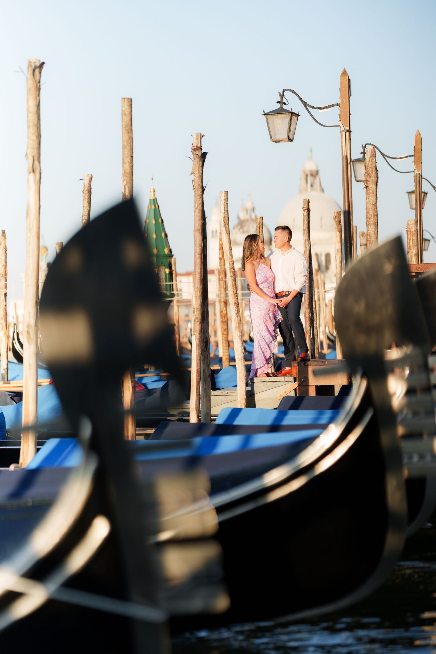 Romantic couple embracing among Venice gondolas and wooden poles at St. Mark's Square waterfront in Italy.