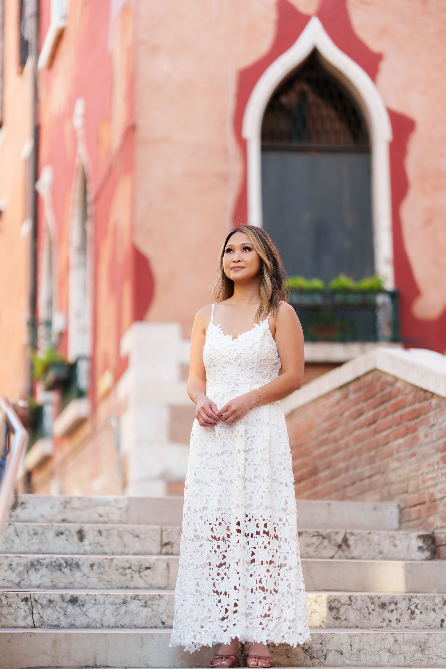 Woman in white lace maxi dress standing on stone steps in Venice, Italy.