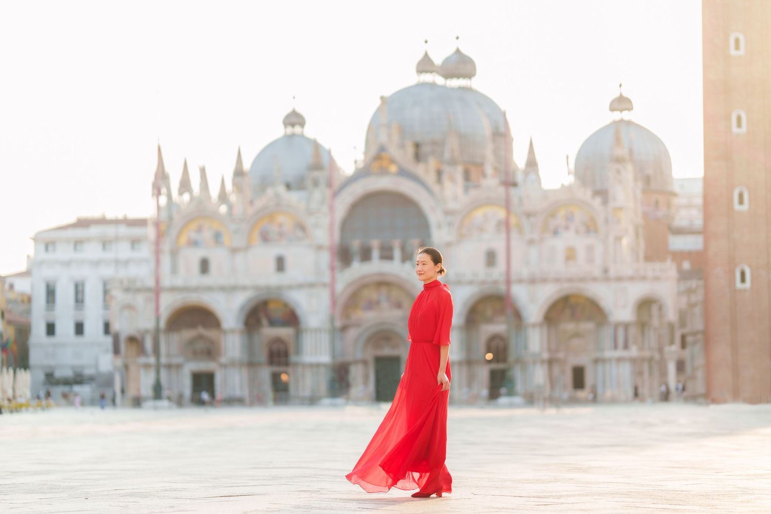 Woman in red gown poses in St. Mark's Square, Venice, with the iconic Basilica di San Marco in the background.