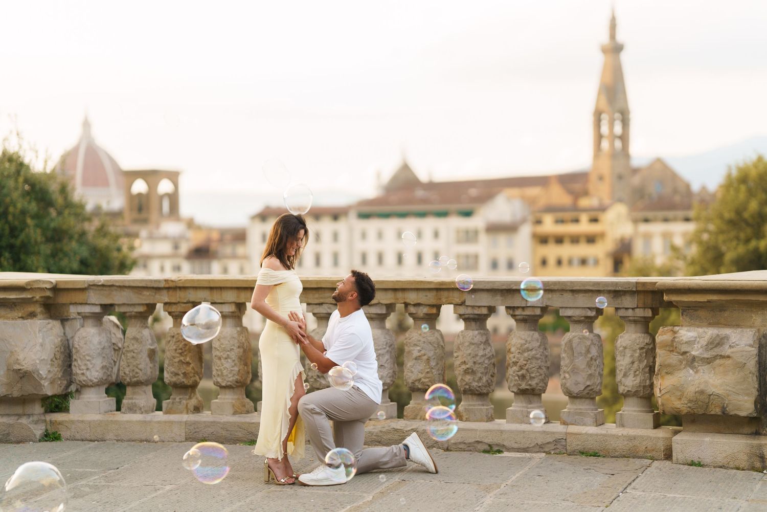 Man proposing to woman on a scenic Florence terrace with bubbles, Duomo and church towers in the background.