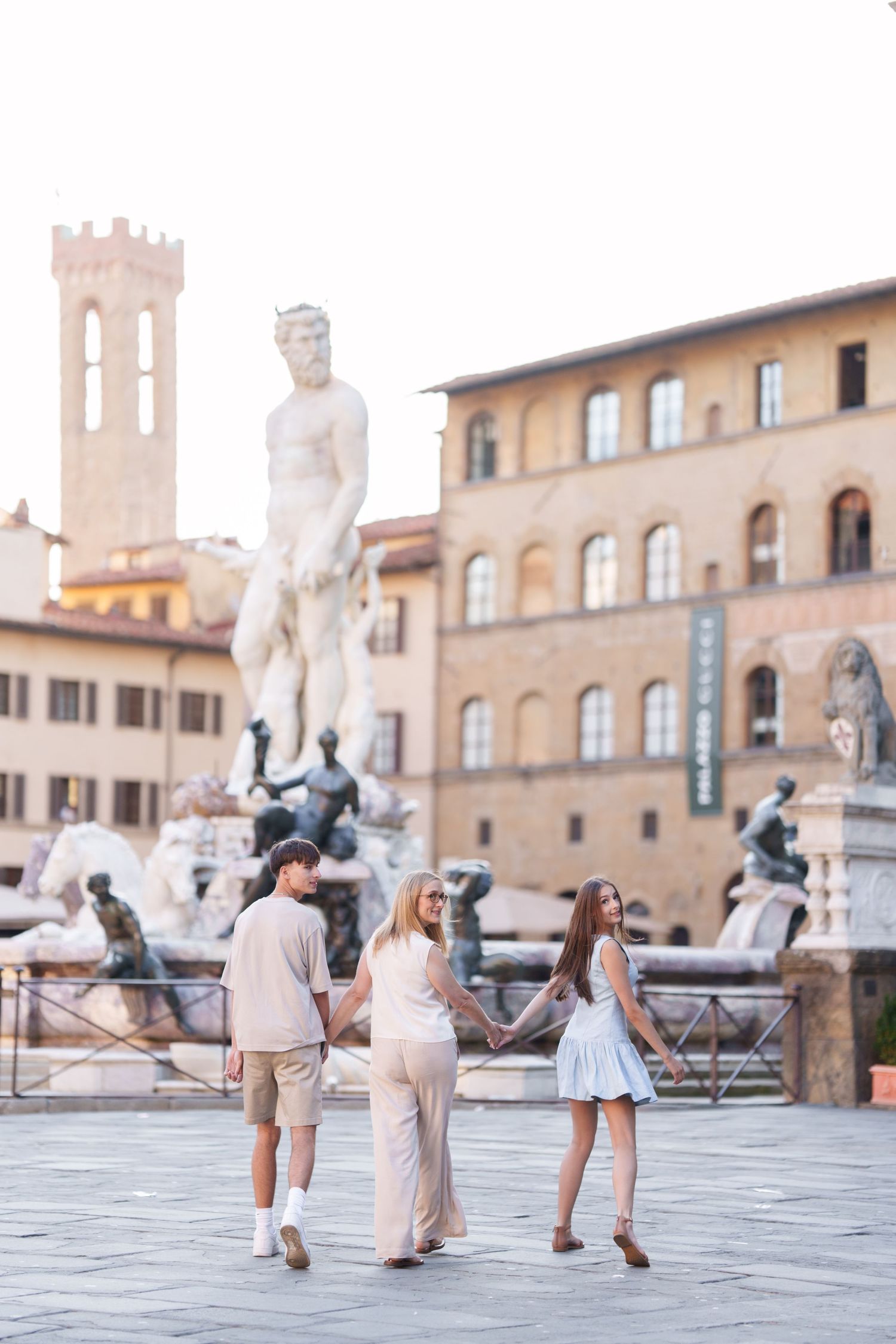 Tourists take photos in front of historic statues at Piazza della Signoria in Florence, Italy during sunset.