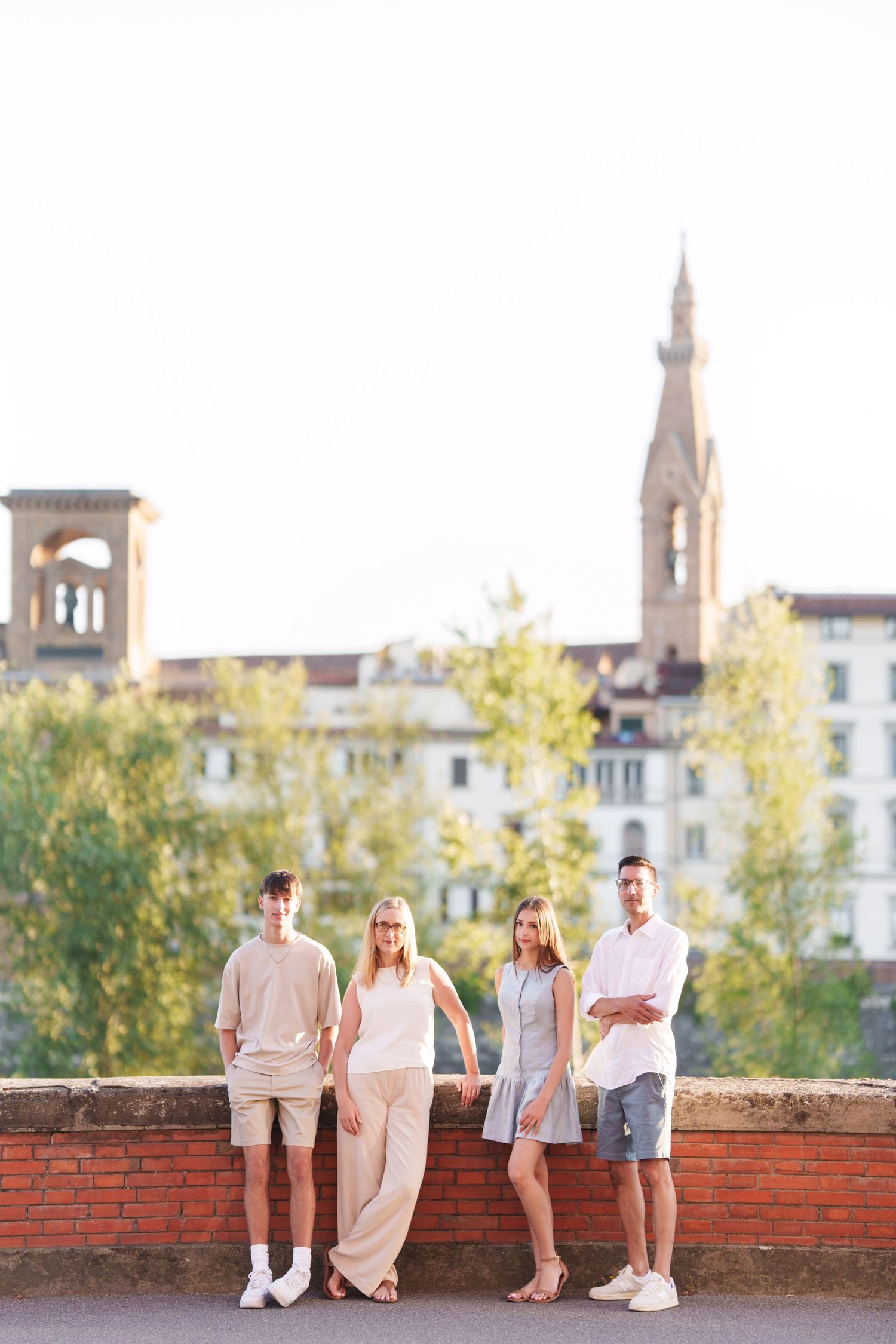 Group in coordinated neutral outfits sitting on brick wall with historic Florence cityscape and church spires in background.