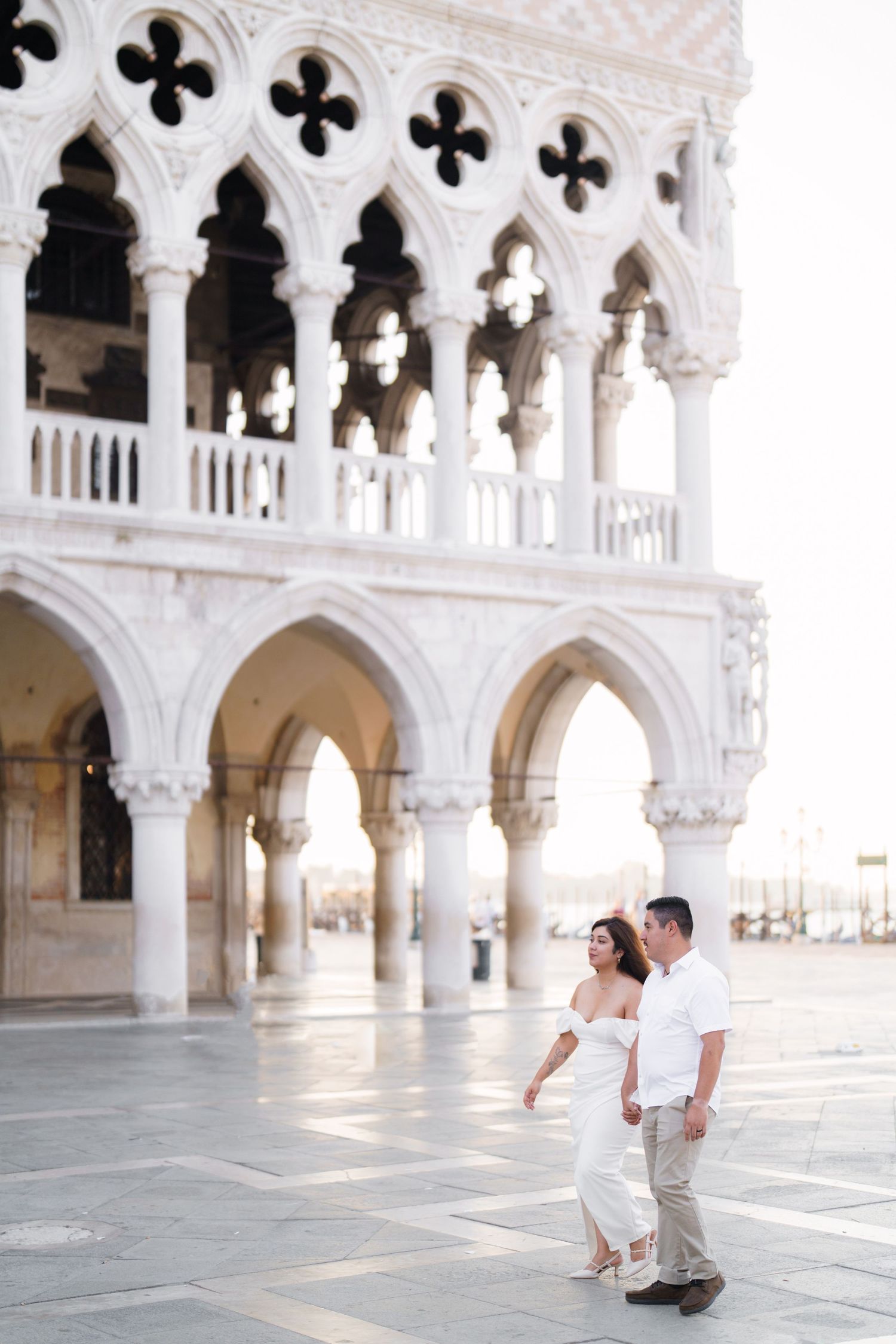 Two people pose together under the elegant Gothic arches of Doge's Palace in Venice, Italy.