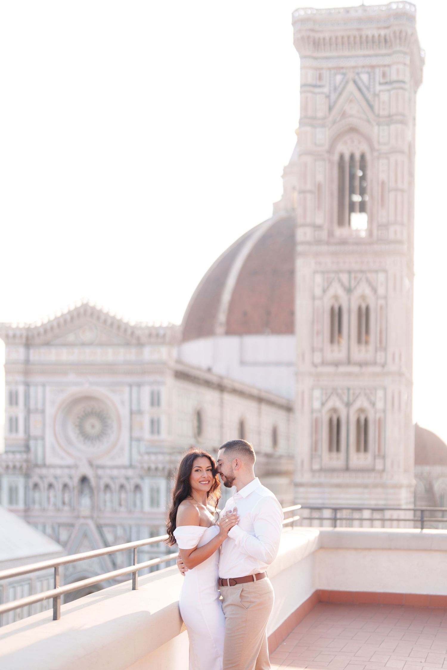 Romantic couple embraces on rooftop terrace overlooking the historic Florence Cathedral and Giotto's Bell Tower in Italy.