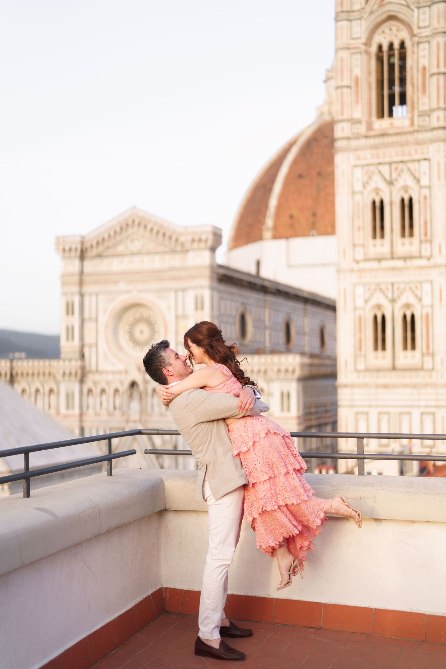 A romantic couple embraces on a rooftop terrace with Florence Cathedral and Brunelleschi's Dome in the background.