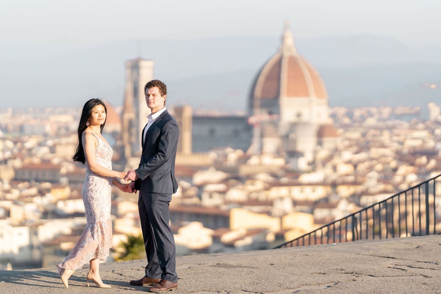 A couple shares a romantic moment at Piazzale Michelangelo overlooking Florence's iconic Duomo cathedral and cityscape.