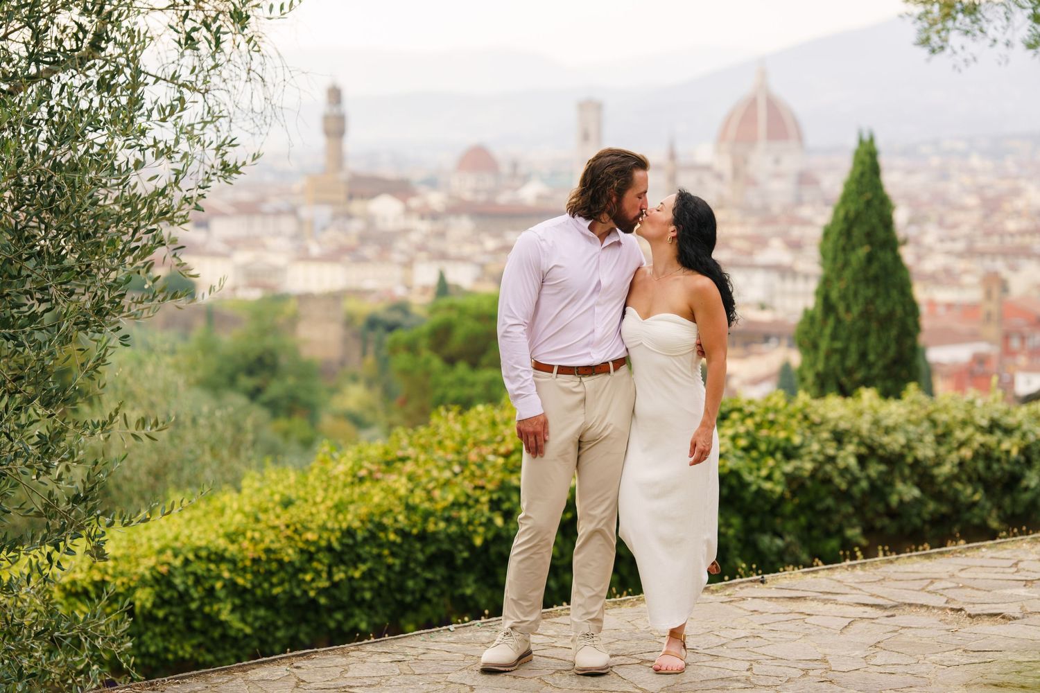 A couple shares a romantic moment overlooking the scenic Florence skyline with the Duomo cathedral visible in the distance.