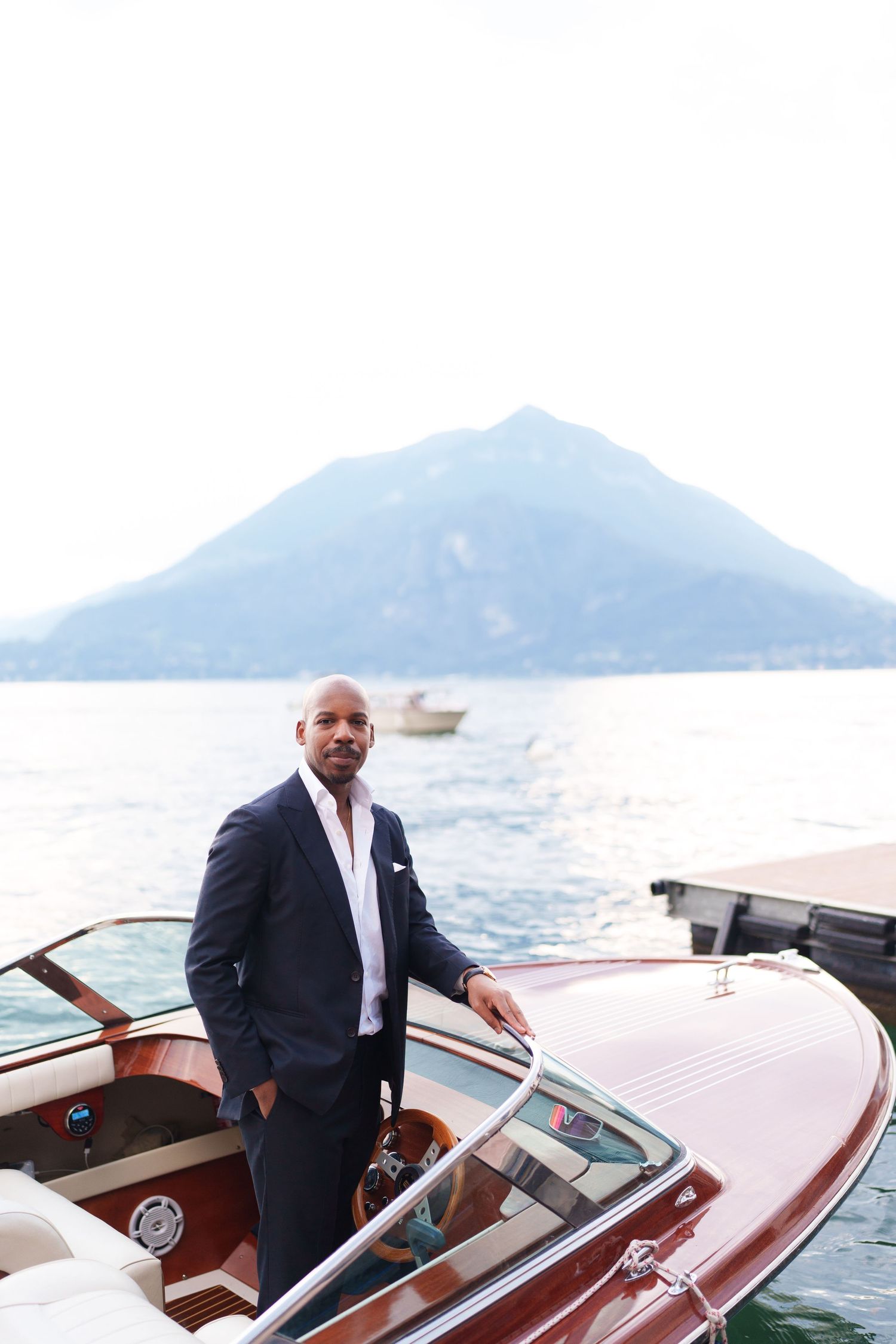 Luxury wooden boat cruising on Lake Como with mountains in background and elegant passengers aboard.