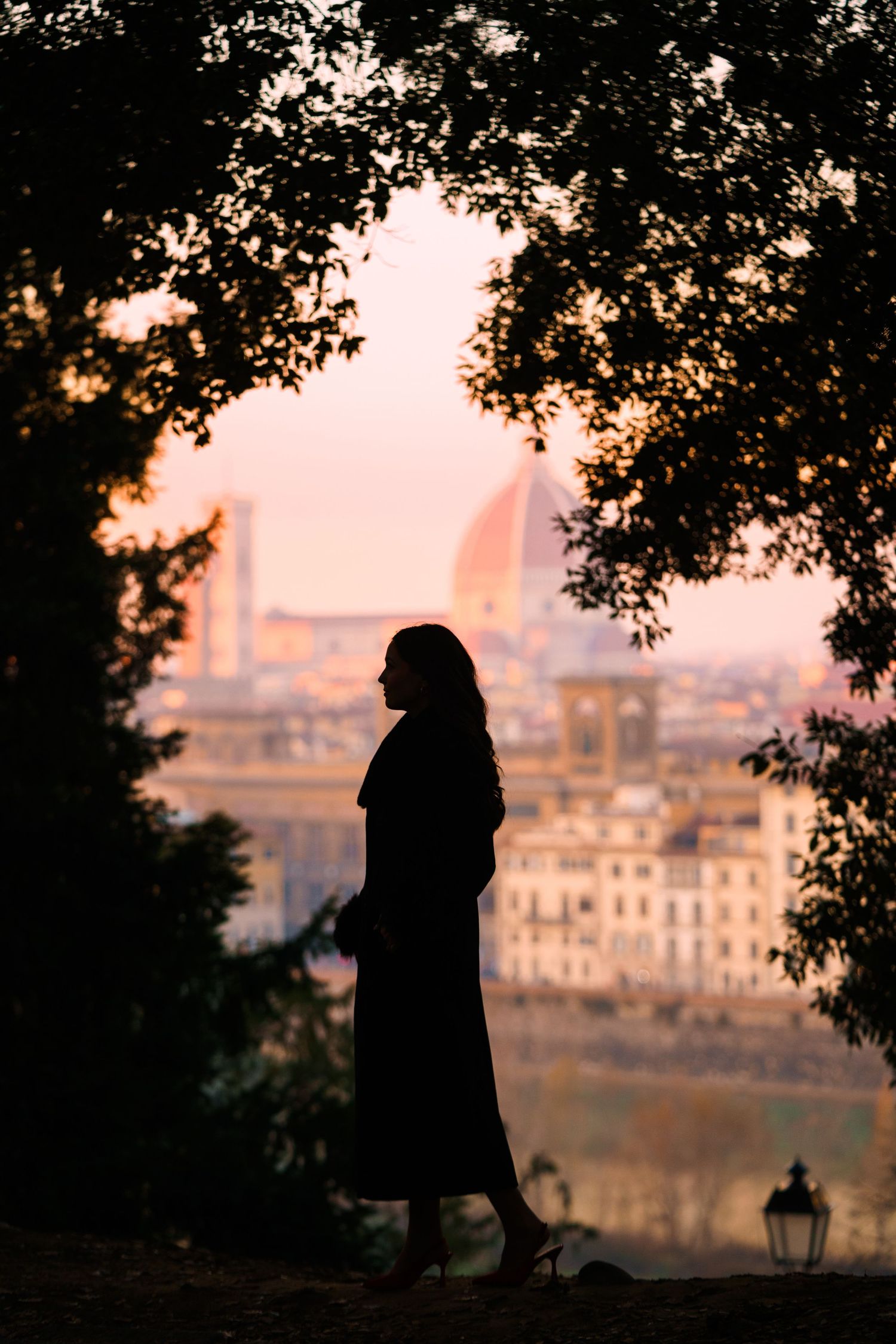 Silhouette of a figure in a long dress against sunset backdrop of Florence cityscape with Duomo cathedral visible.