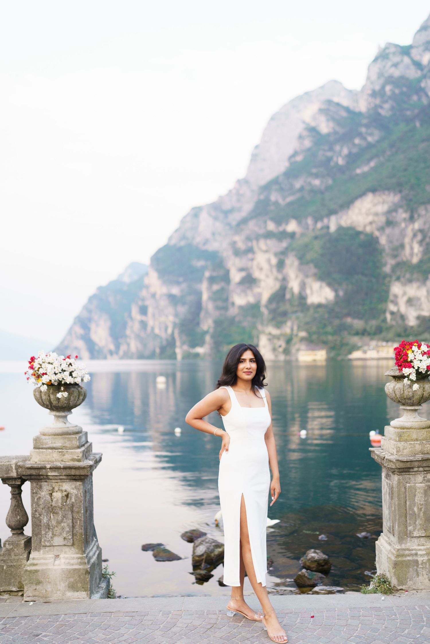 Elegant white dress photoshoot by Lake Garda in Italy with dramatic mountain backdrop and stone pillars with flowers.