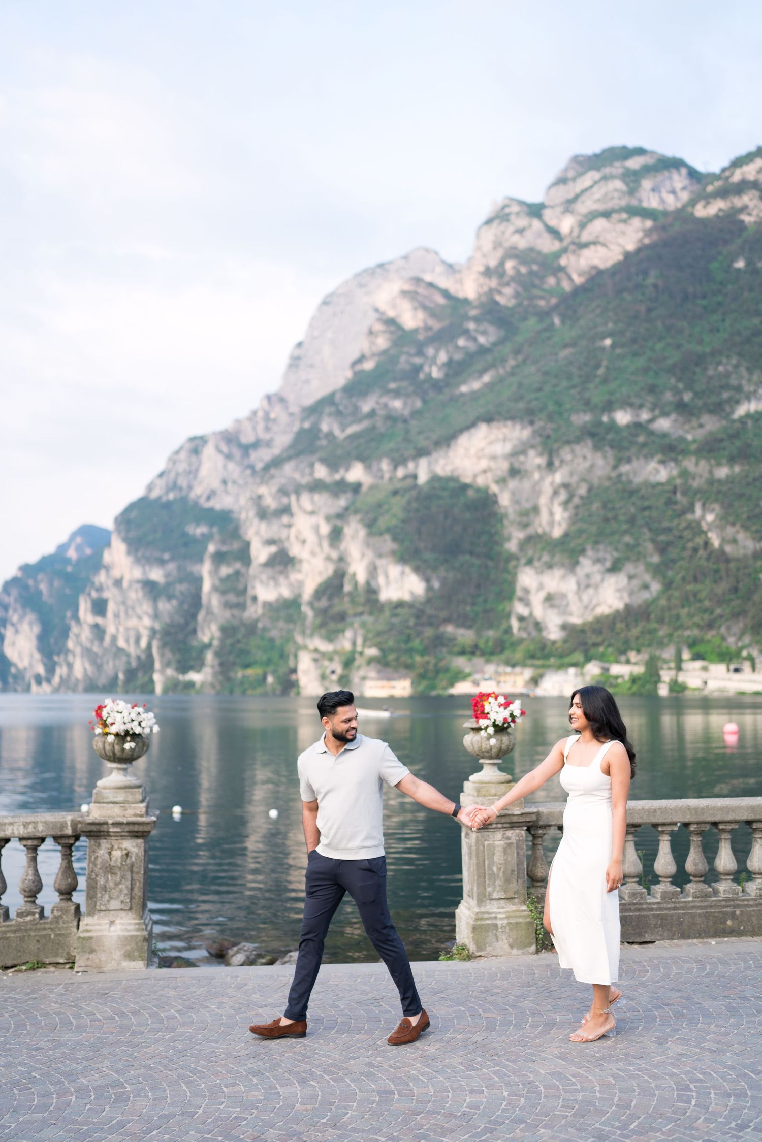 Couple dancing on lakeside promenade with dramatic mountain cliffs and Lake Garda scenery in Riva del Garda, Italy.