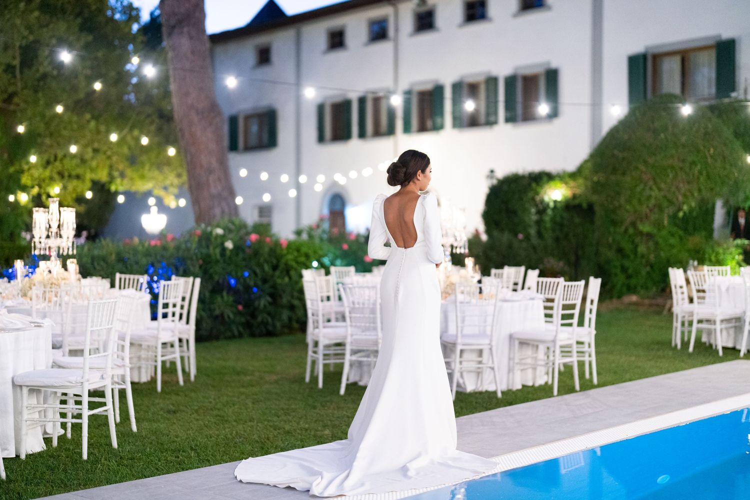 Elegant wedding reception setup with white chairs and twinkling lights around a pool at a luxurious villa.