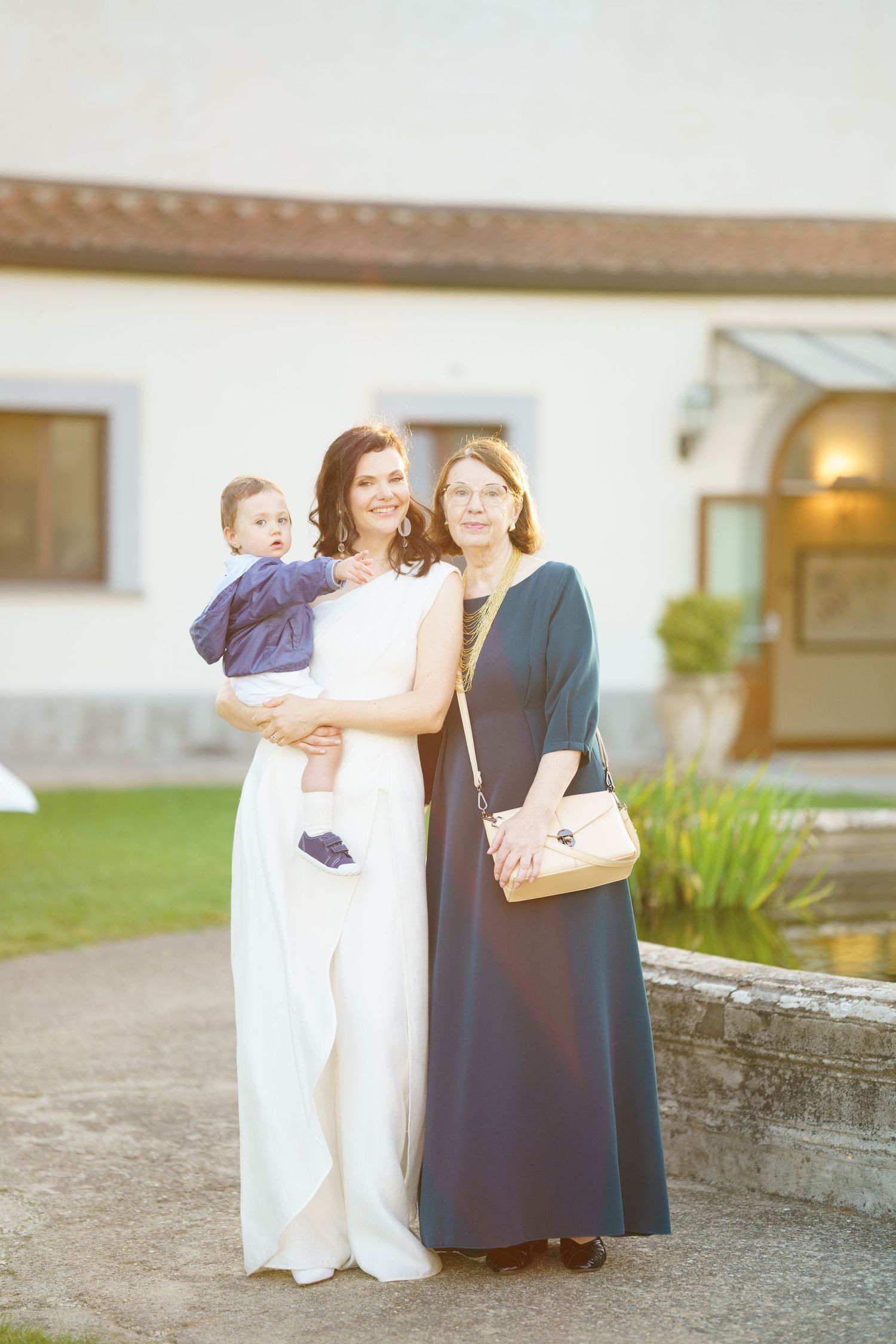 Three people stand together on stone path outside building during evening event.