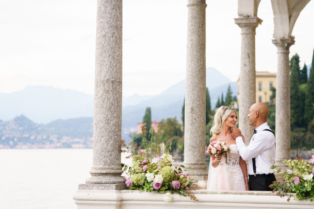 Romantic moment captured under ornate stone colonnade with lake and mountain views.