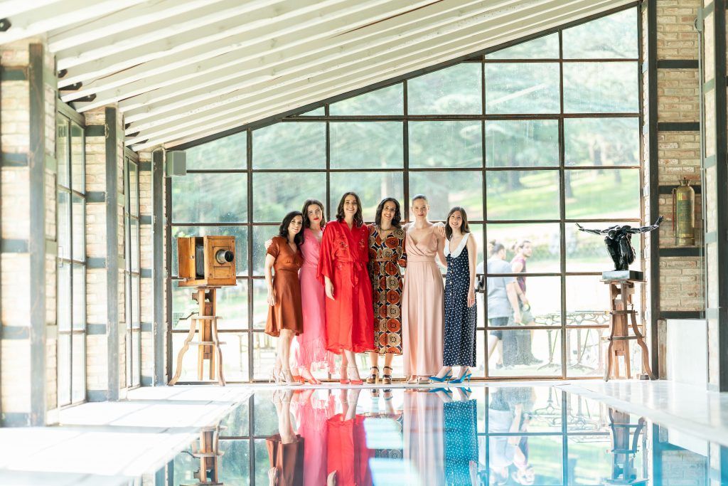 Group photo reflection in modern glass-enclosed space with coordinated formal dresses.