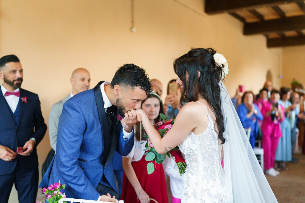 A tender moment during a wedding ceremony with guests watching in a rustic venue decorated with pink flowers.