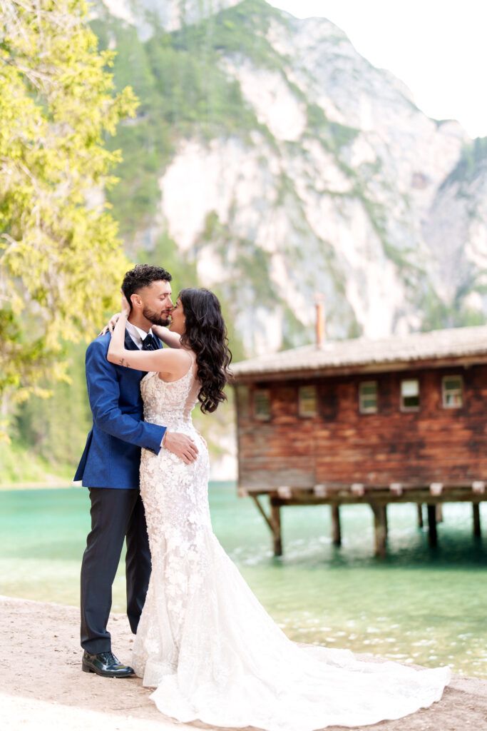 Romantic dance on lakeside dock with mountain backdrop and wooden boathouse.