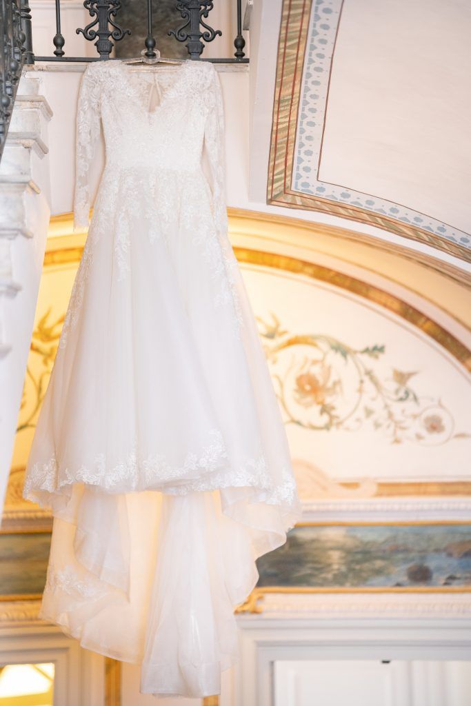 White wedding gown hanging against ornate wall with gilded architectural details.
