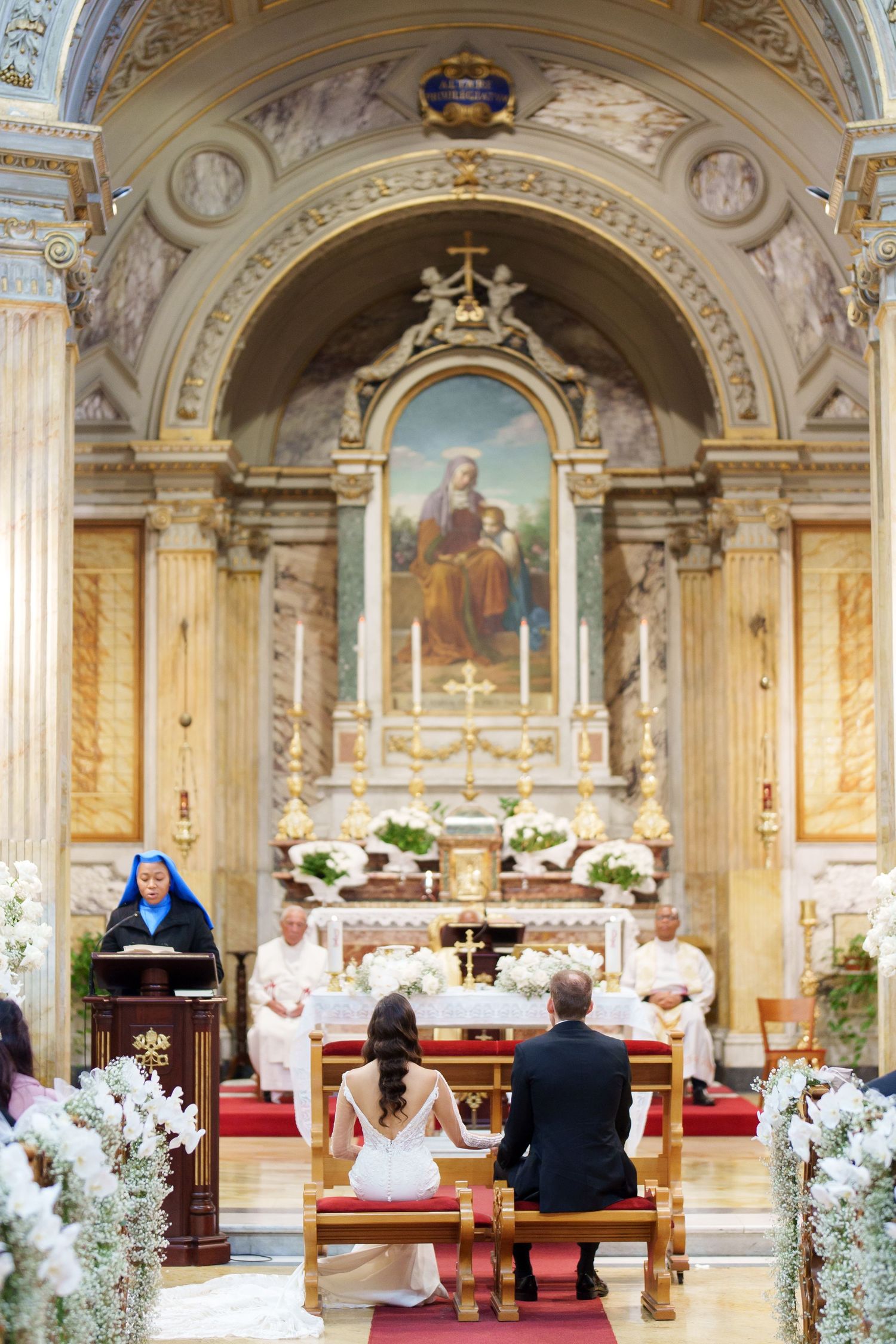 A Catholic wedding ceremony with floral decorations and religious artwork in a grand church setting.