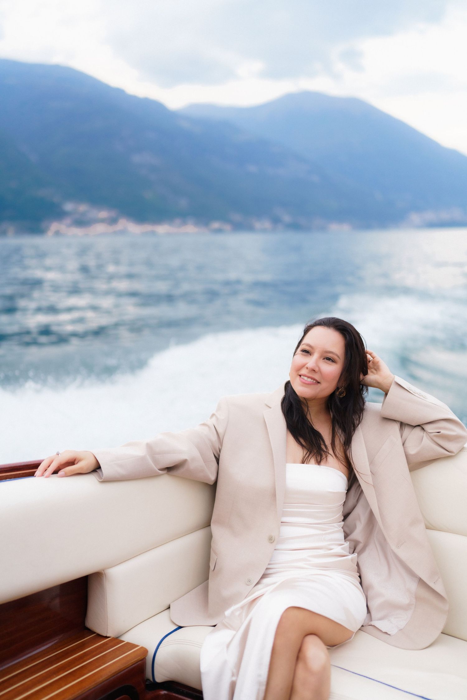 Elegant woman relaxing on a boat deck with mountains and lake in the background on a cloudy day.