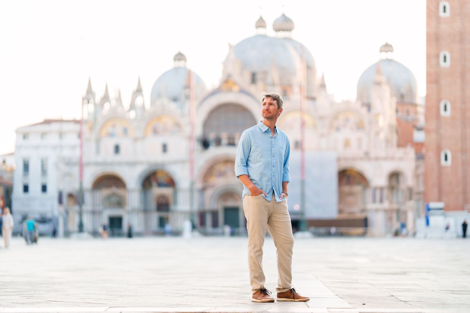 Man standing in St. Mark's Square, Venice, with the iconic Basilica di San Marco in the background on a sunny day.