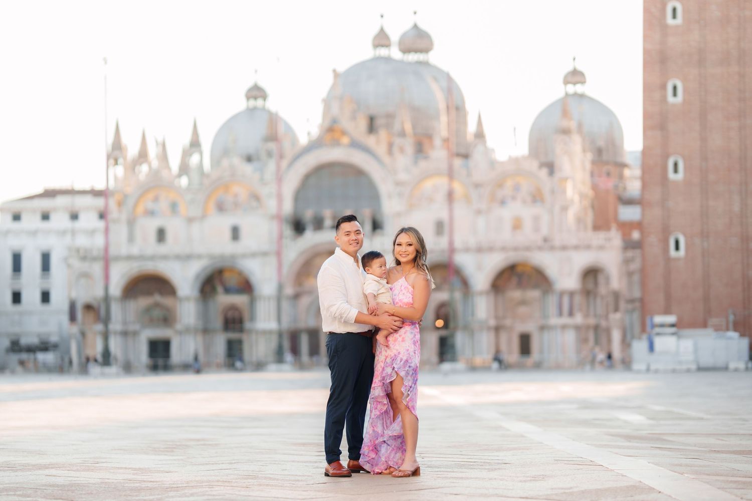 Family posing in St. Mark's Square, Venice, with the iconic Basilica di San Marco in the background at golden hour.