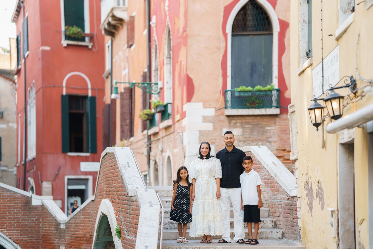 Family of four posing on bridge steps in Venice, Italy, surrounded by colorful historic buildings.
