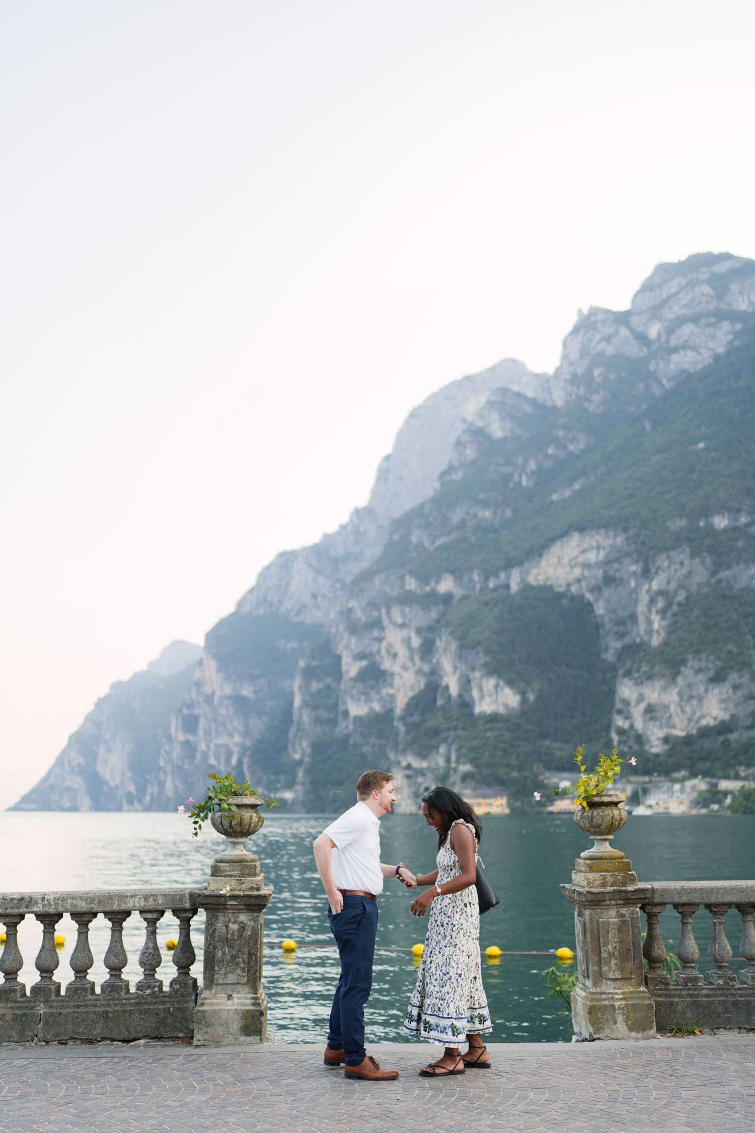 Couple exchanging flowers on elegant stone terrace overlooking Lake Garda and mountains.