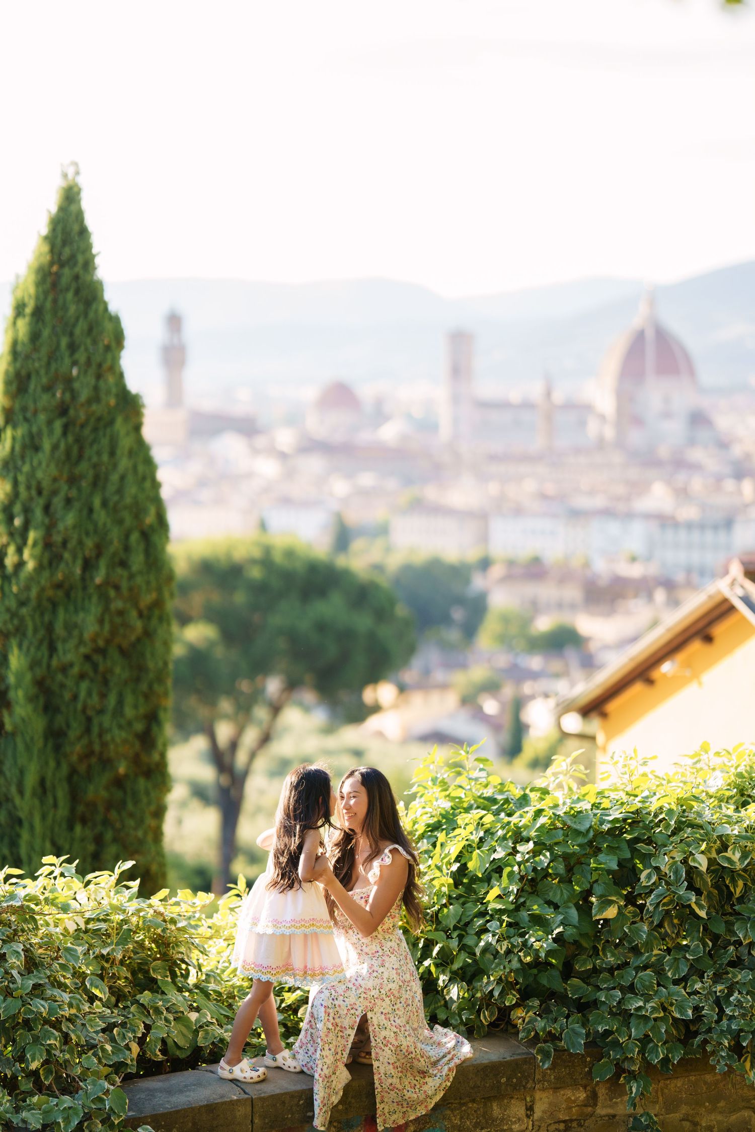 Mother and daughter in elegant dresses pose on a terrace overlooking Florence skyline with the Duomo in background.