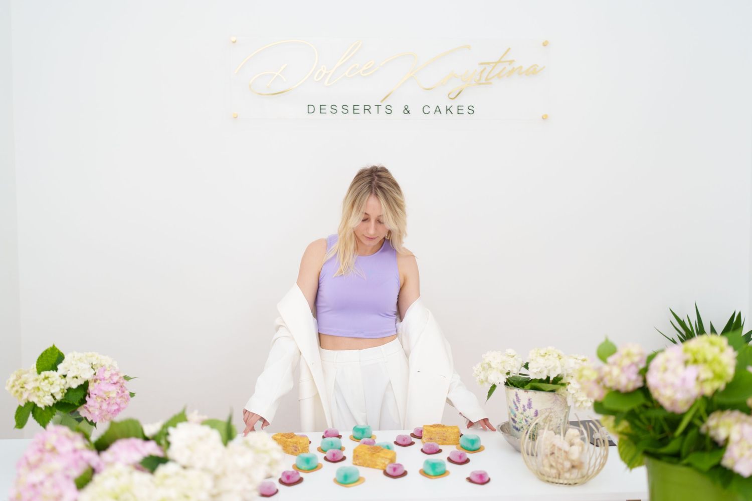 Woman in lavender crop top arranging colorful macarons on a dessert table at a cake and dessert shop.