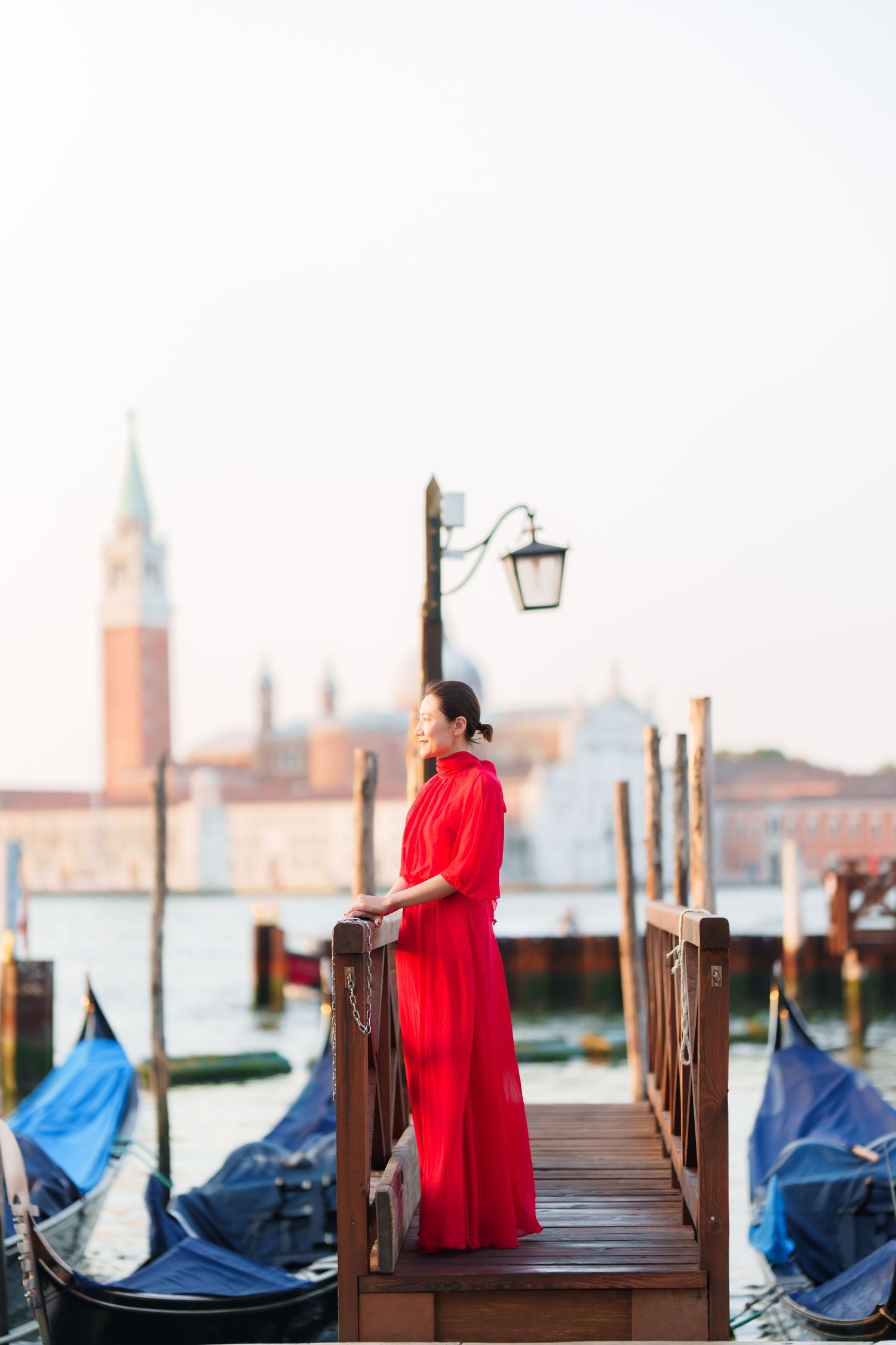Woman in red dress standing on Venice gondola dock with San Giorgio Maggiore church in background.