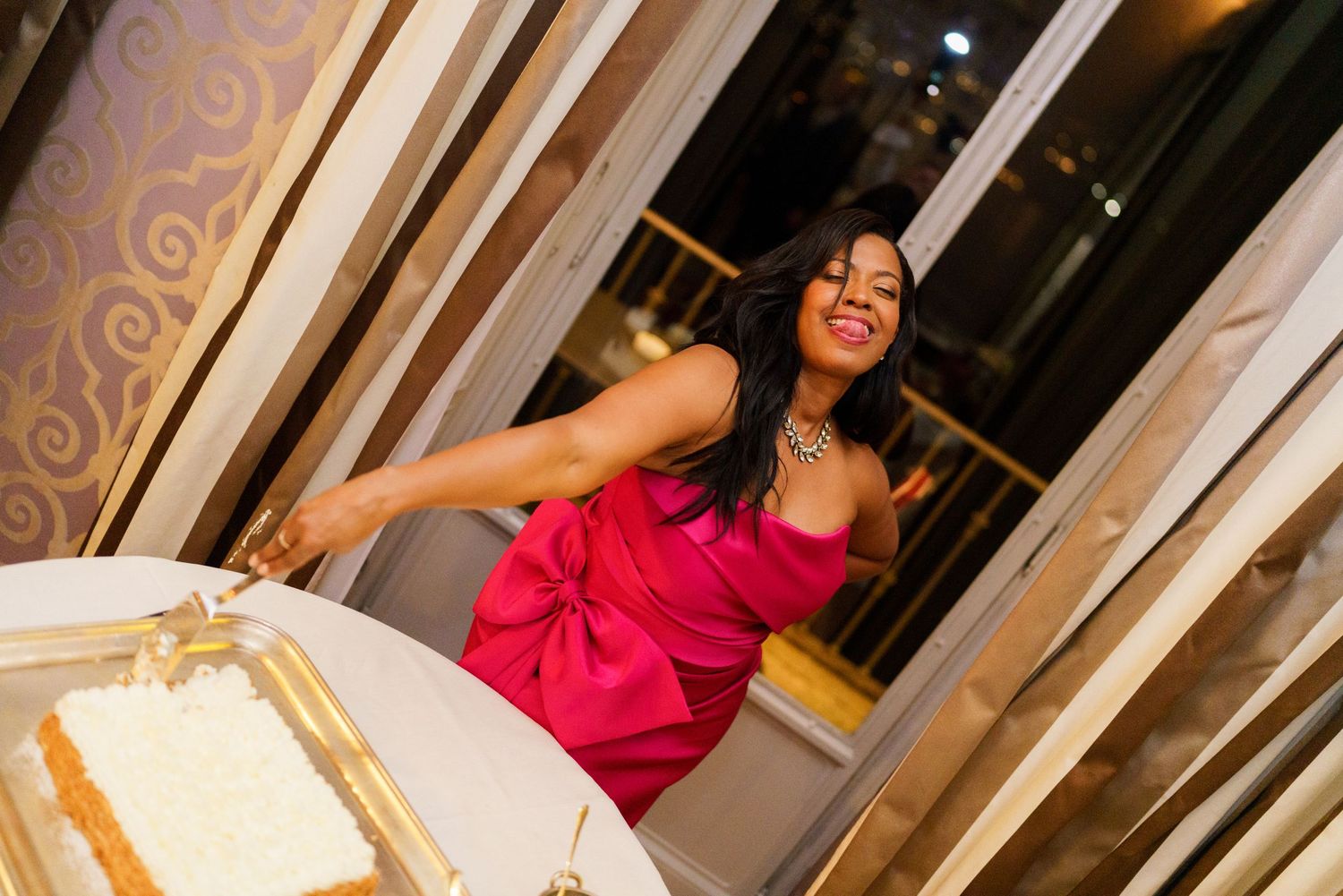 Woman in pink dress cutting white cake at elegant celebration event.