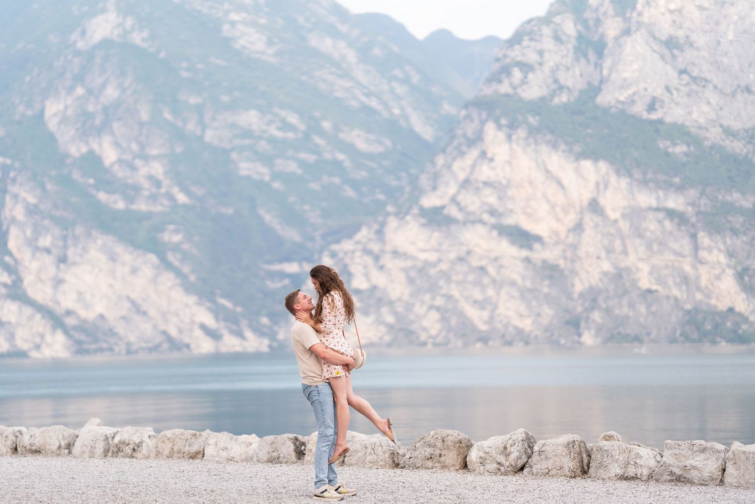 Couple embracing by a serene lake with dramatic mountain backdrop, romantic outdoor moment.