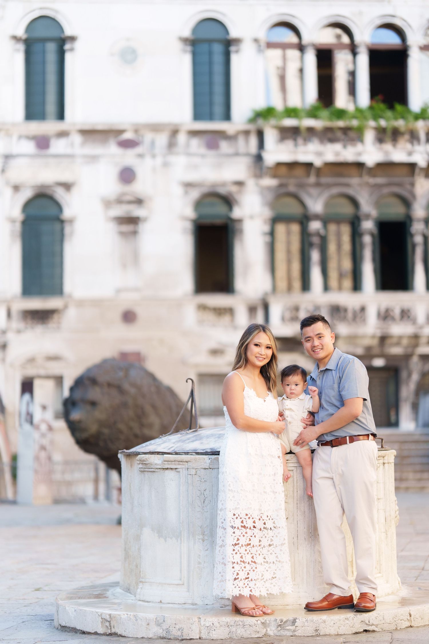 Family of three posing by a stone well in Venice, Italy, with historic architecture in the background.